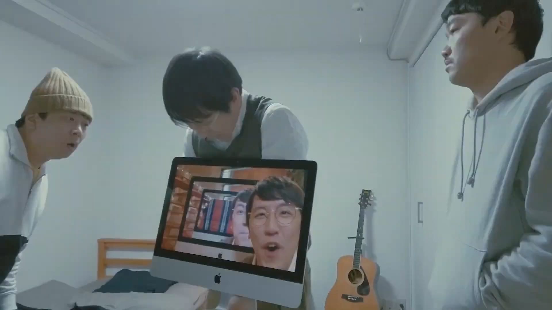 A Japanese man holds an Apple monitor showing his own face in two iterations, while two other Japanese men look up