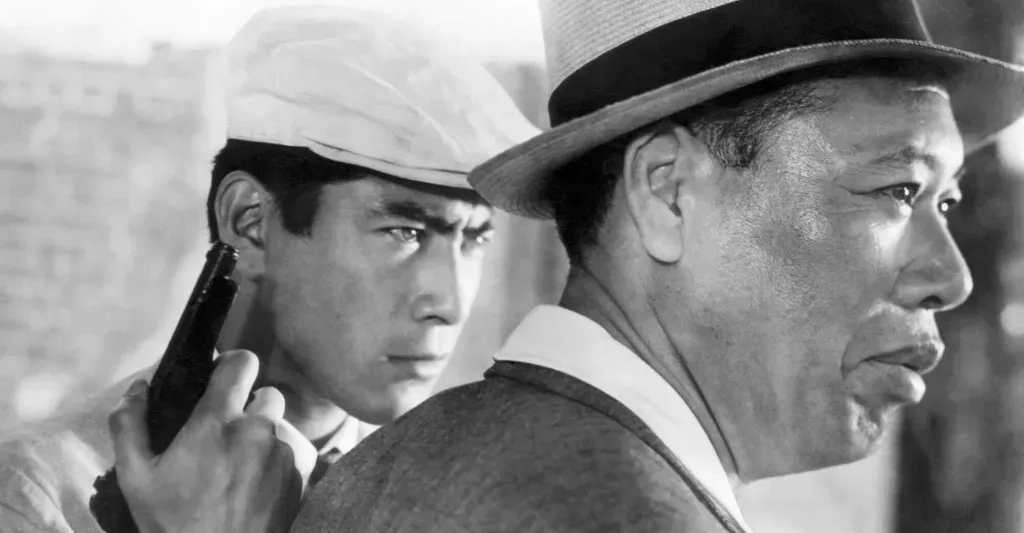 Still from Stray Dog showing Toshiro Mifune in a white flat cap holding a gun beside Takashi Shimura. Both men look off to the right.