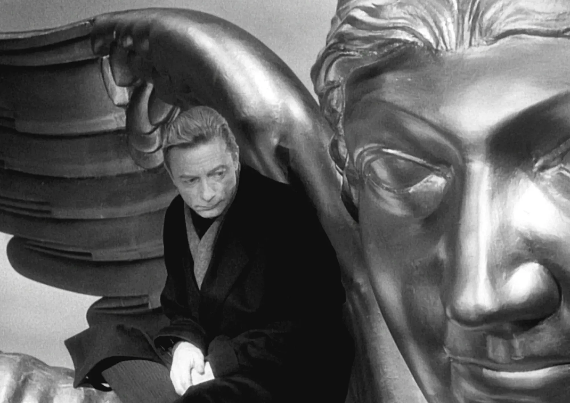 Still from Wings of Desire showing Otto Sander sitting on the shoulder of massive gilded statue of an angel.