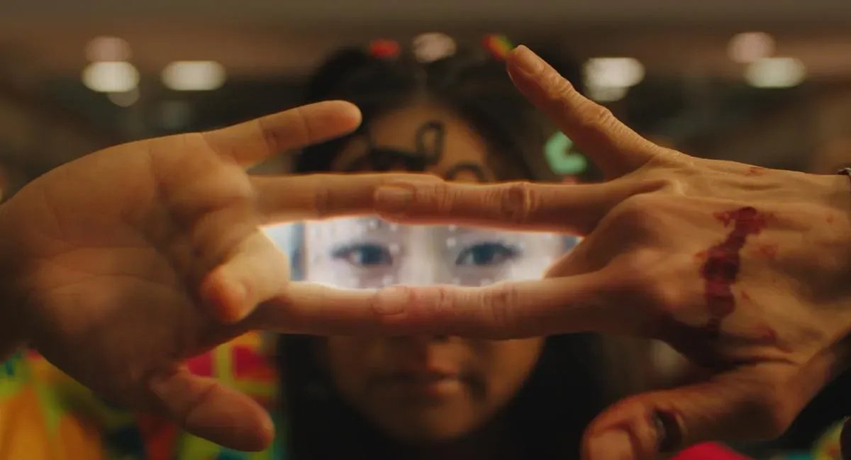 Bloodied hands form a window with their fingers through which they show an alternate universe Stephanie Hsu