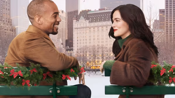 Kendrick Sampson and Zoey Deutch sit smiling at each other on festooned park benches in the snow