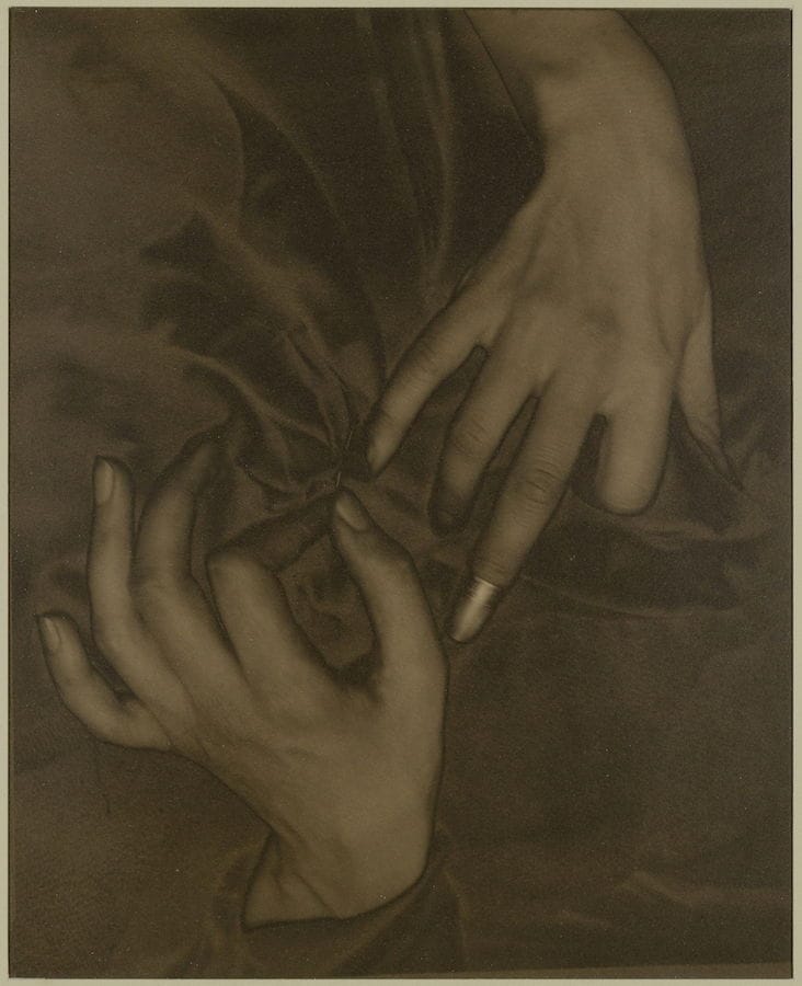 Sepia photograph of a woman's hands in fabric, with a thimble on one index finger